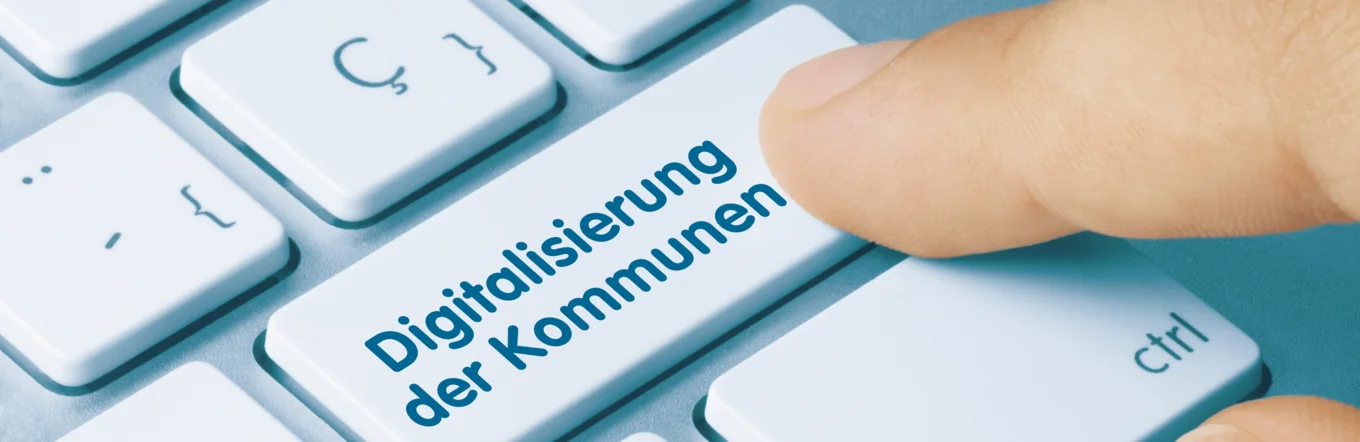 Zeigefinger betätigt Taste mit Text „Digitalisierung der Kommunen" auf weißer Computertastatur