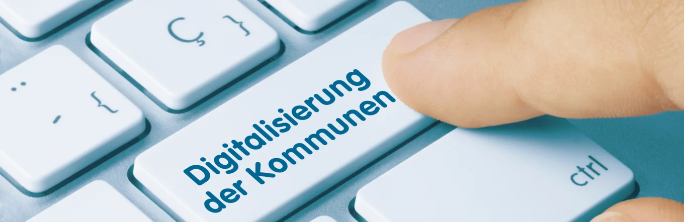 Zeigefinger betätigt Taste mit Text „Digitalisierung der Kommunen" auf weißer Computertastatur