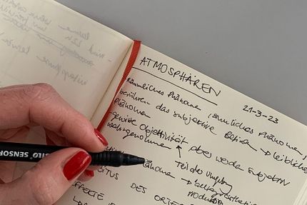 Eine Hand hält einen Stift und schreibt Notizen in ein Notizheft.