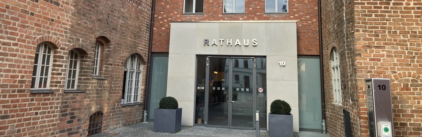 Eingang eines Rathauses mit Glasportal, Schriftzug und gepflastertem Innenhof