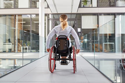 Frau im Rollstuhl im Flur eines Bürogebäudes