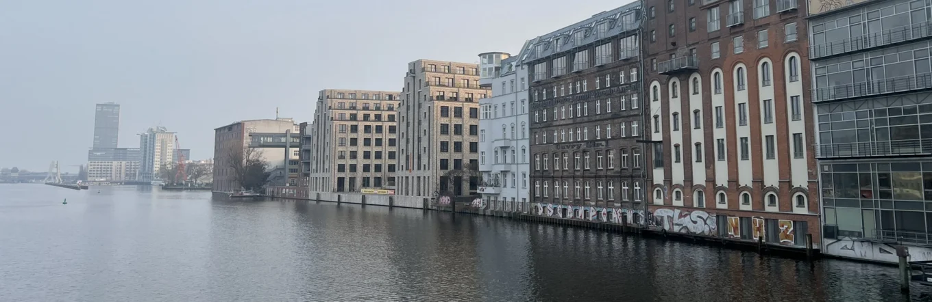 Berliner Spreeufer mit heterogener Bebauung aus Gründerzeit, Industriebauten und Neubauten bei bedecktem Himmel