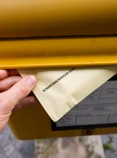 Zu sehen ist die Nahaufnahme einer Hand, die einen Umschlag mit der Aufschrift "Kommunalwahlen 2024" in einen Briefkasten steckt