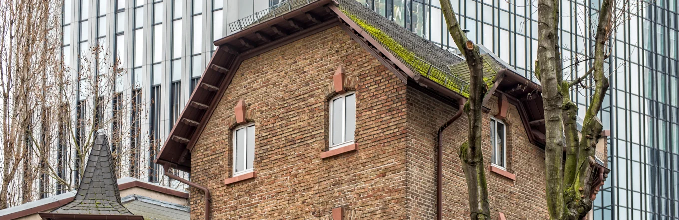 Historisches Backsteingebäude mit Fachwerkerker vor spiegelnder Glasfassade eines Hochhauses