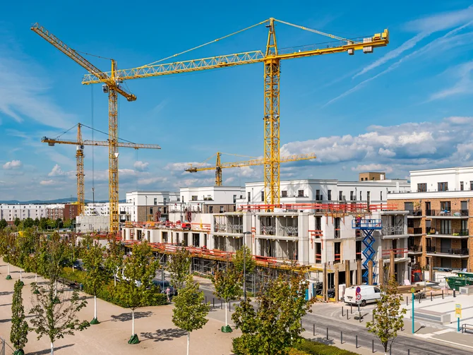 Öffentliches Baurecht Wachsendes Stadtquartier mit Wohnhäusern im Rohbau, Baukränen und begrünten Erschließungsstraßen