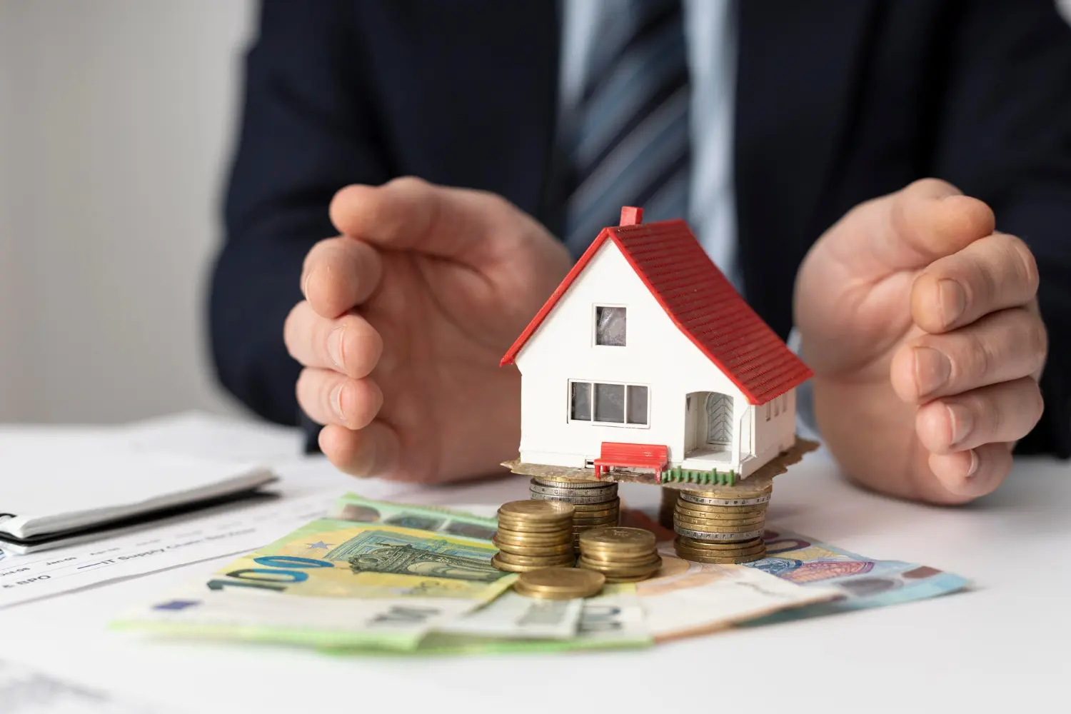 Einstieg ins Wohngeldrecht Person schiebt ein kleines Haus mit Geld zur Kamera.