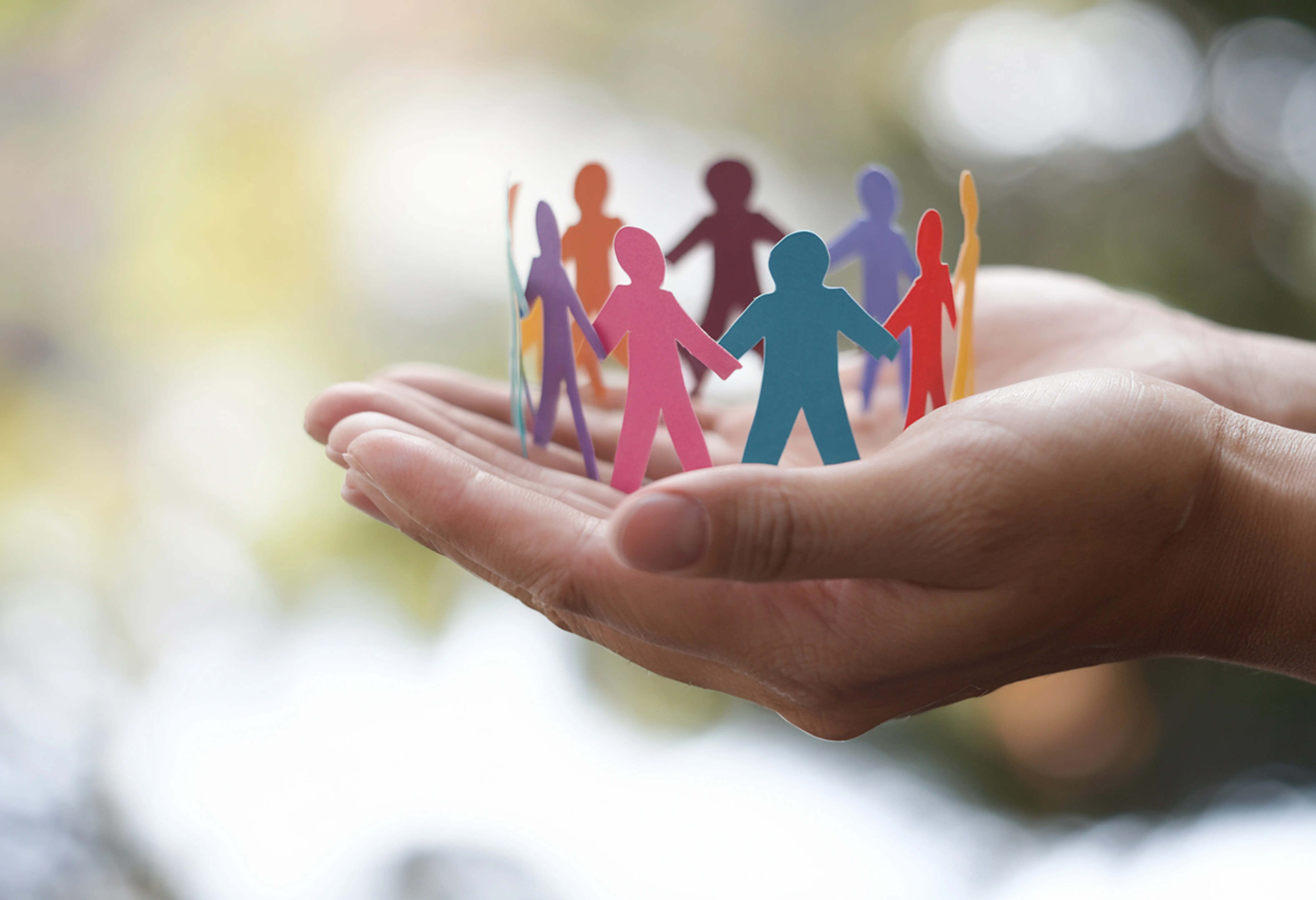 wohngeld-und-sozialrecht-c-arshadul-adobestock Zwei Hände halten einen Kreis bunter Papiermenschen-Figuren als Symbol fuer Gemeinschaft und Fuersorge
