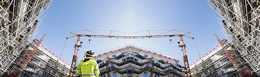 Bauleiter im Vorderungrund einer Großbaustelle mit Rohbauten im Hintergrund.
