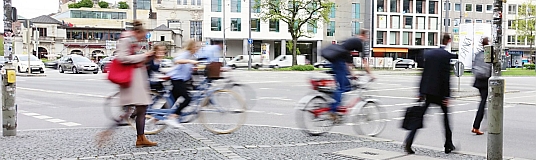 Beispiel für Verkehrsplanung: Eine Straßenkreuzung mit viel Verkehr, verschwommenen Fußgängern und Radfahrern, die sich schnell bewegen.