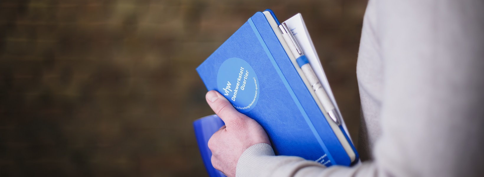 Mensch hält Buch im Arm auf dem steht "Denkwerkstatt Quartier"