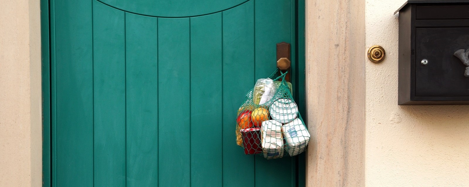 Beutel gefüllt mit Lebensmitteln hängt außen an einer geschlossenen Haustür.