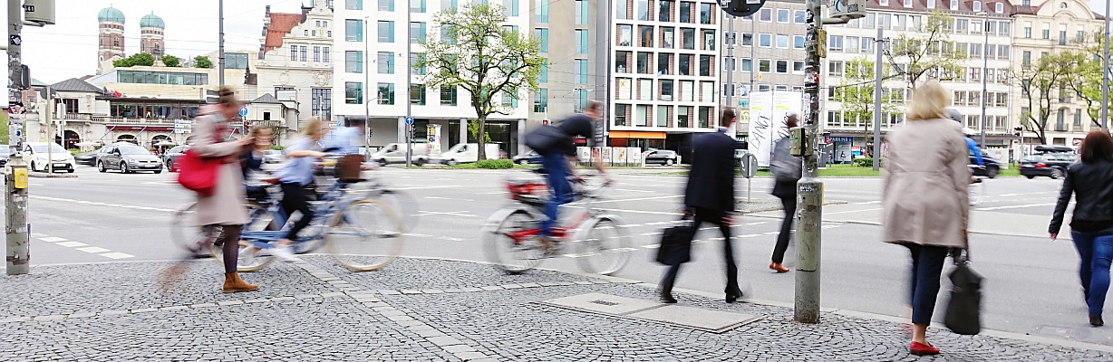 Beispiel für Verkehrsplanung: Eine Straßenkreuzung mit viel Verkehr, verschwommenen Fußgängern und Radfahrern, die sich schnell bewegen.