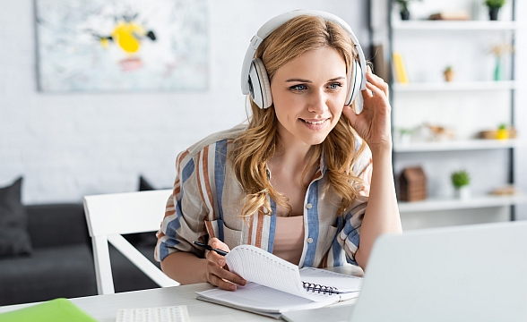 vhw-Webinare © LIGHTFIELD STUDIOS/stock.adobe.com Junge Frau nimmt zuhause an einem Webinar mit Laptop und Kopfhörer teil.
