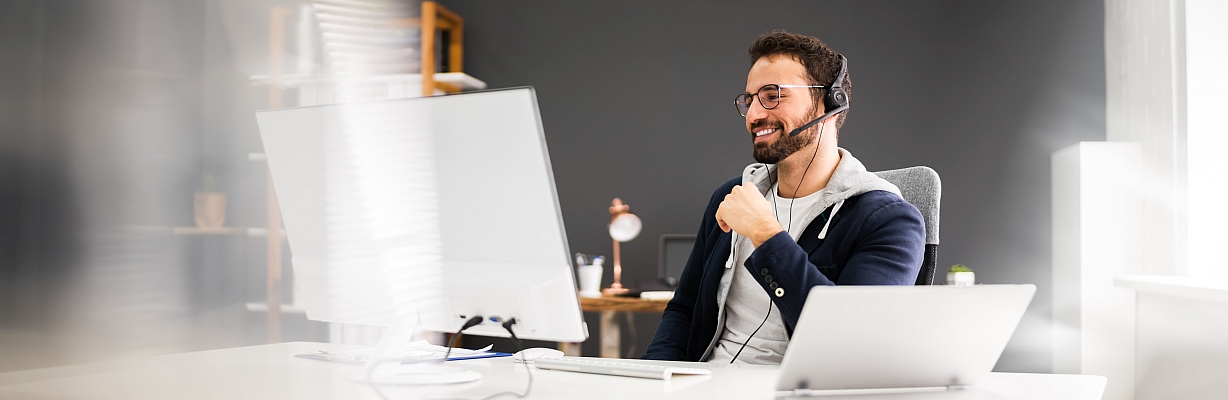 Junger Mann mit Headset nimmt im Büro über seinen Computer an einem Webinar teil.