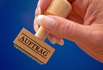 Foto einer Hand, die einen Stempel festhält mit der Aufschrift "Auftrag"